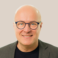 Dr. Mathias Höschel trägt einen dunklen Anzug und ein schwarzes T-Shirt vor hellem Hintergrund