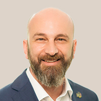 Dr. Christian Klarmann trägt einen dunklen Anzug, weißes Hemd und hat einen kurzen Bart